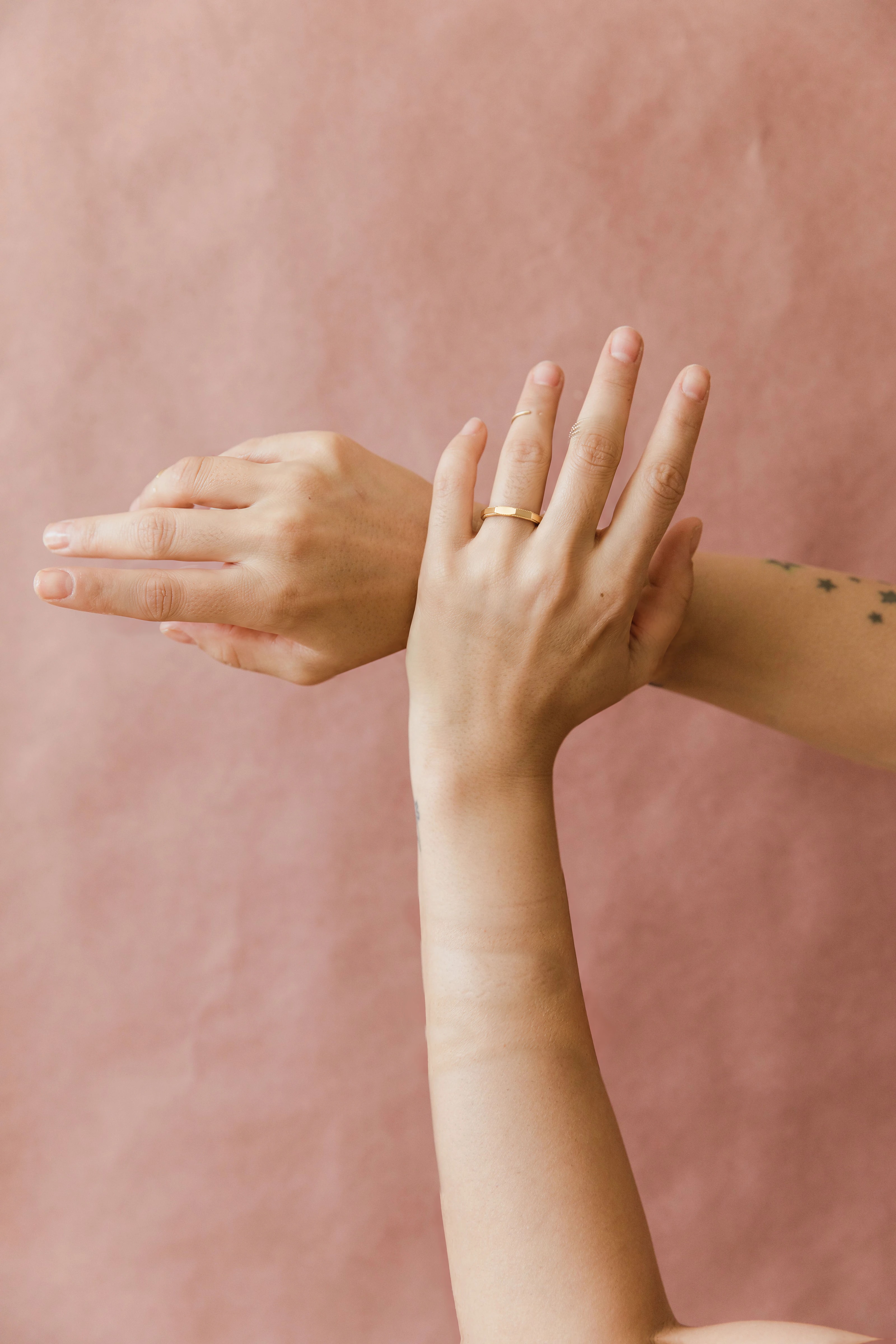 Hands crossed at the wrist on a blush backdrop, wearing the VÉRA Orra Band