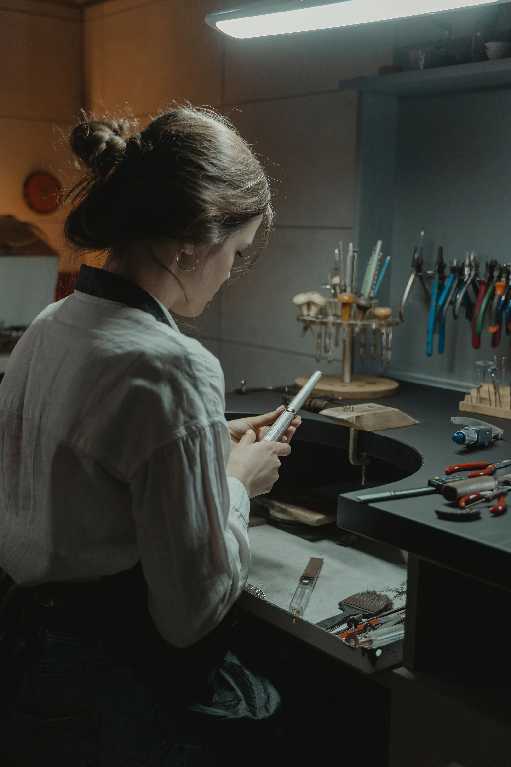 A goldsmith at her bench, surrounded by pliers and files