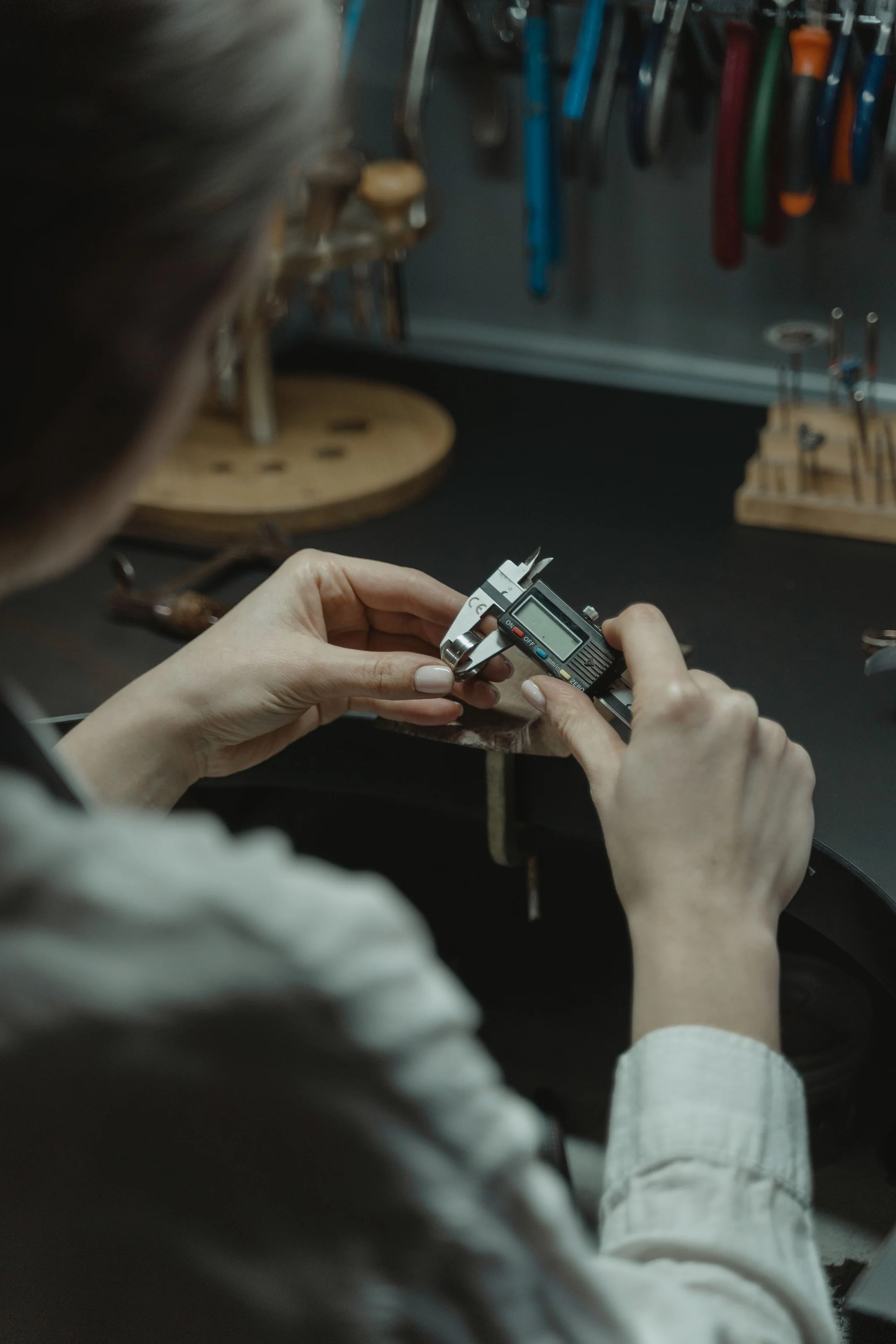 Hands measuring a gold ring with digital calipers at the jeweler's bench