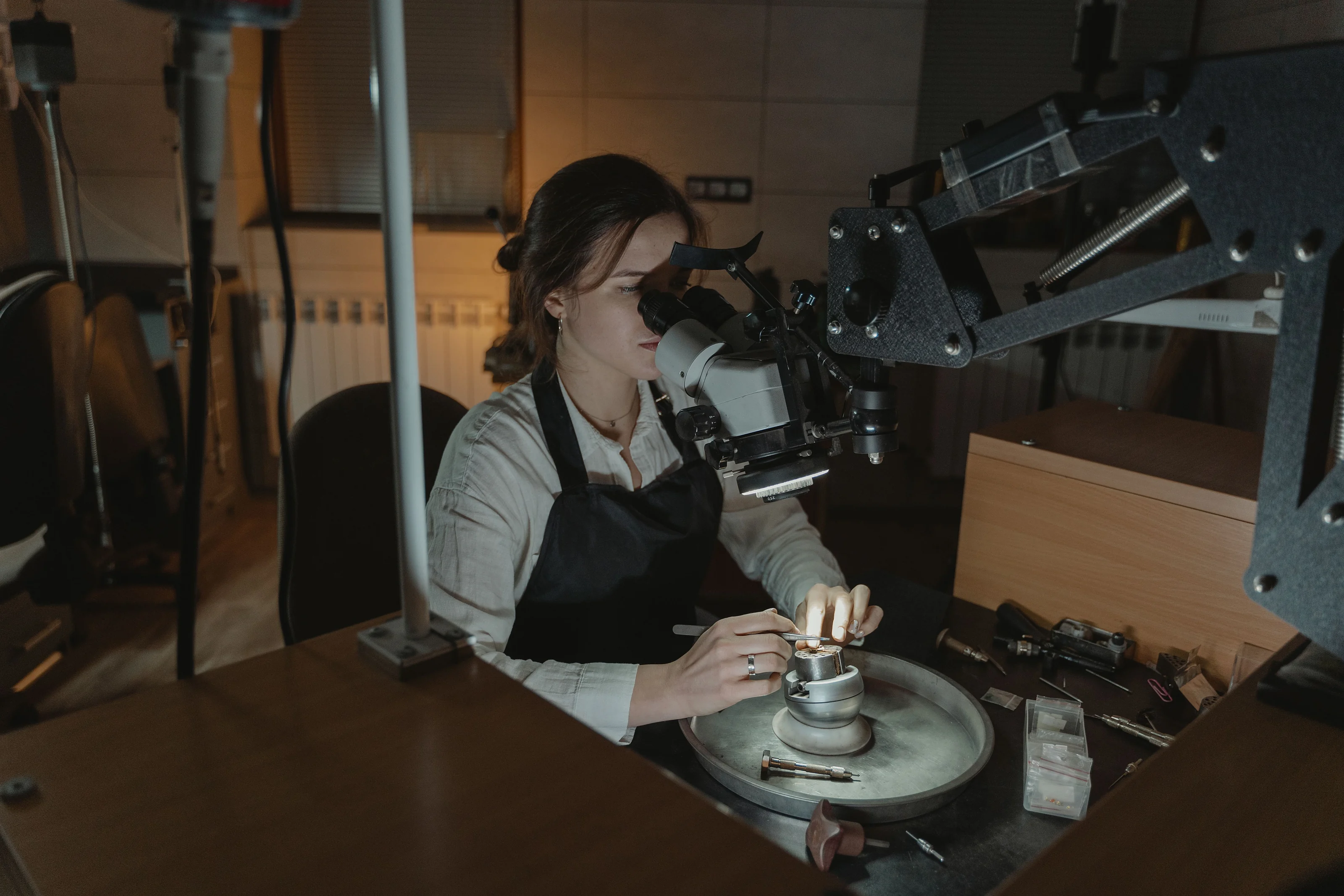 A goldsmith inspecting a piece under a bench microscope in the studio