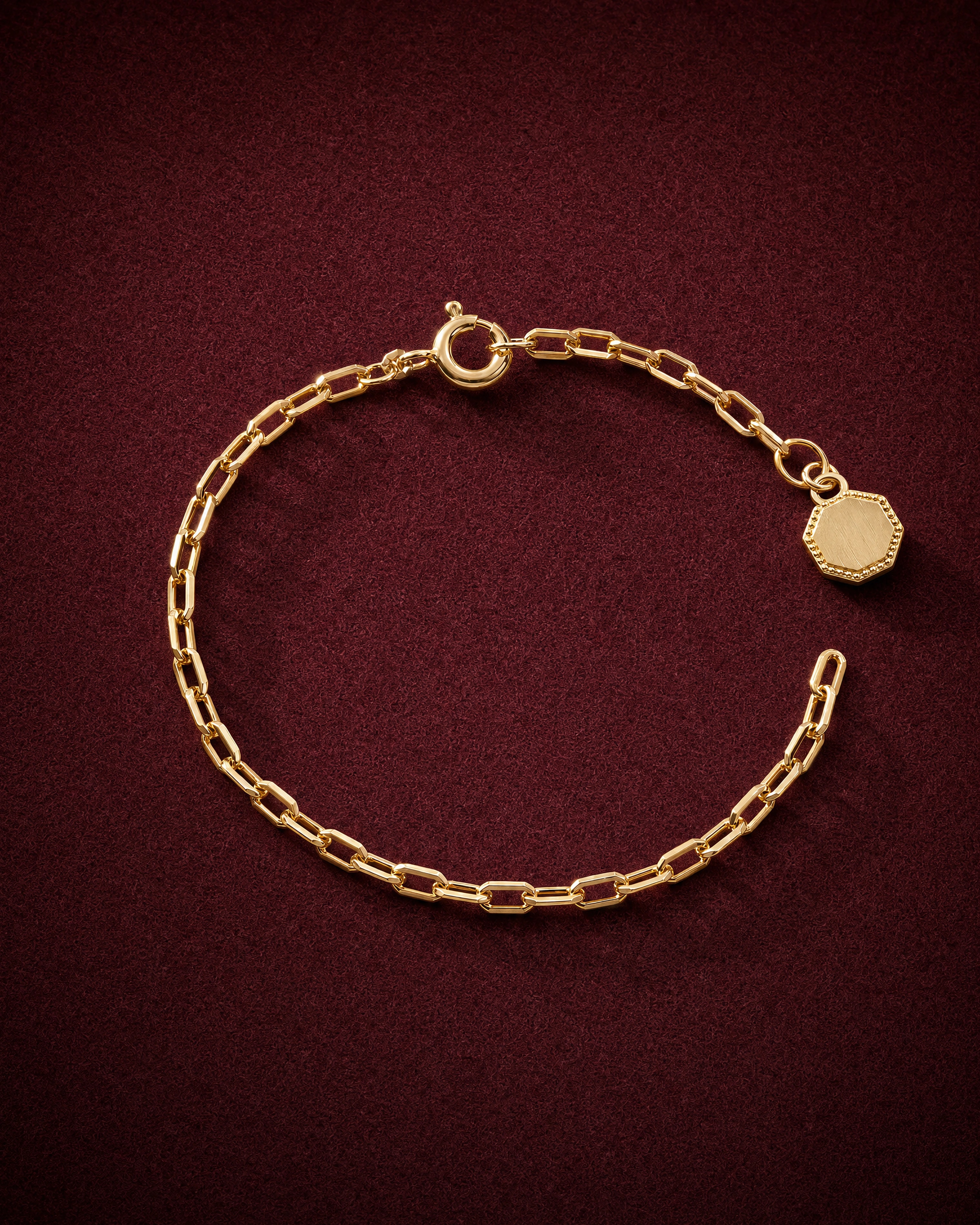 Fil Chain Bracelet of octagonal gold links with an octagonal hallmark tag, on garnet jeweler's felt